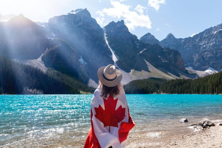 Woman with Canadian flag around back looking at Rocky Mountains Alberta mountains and lake