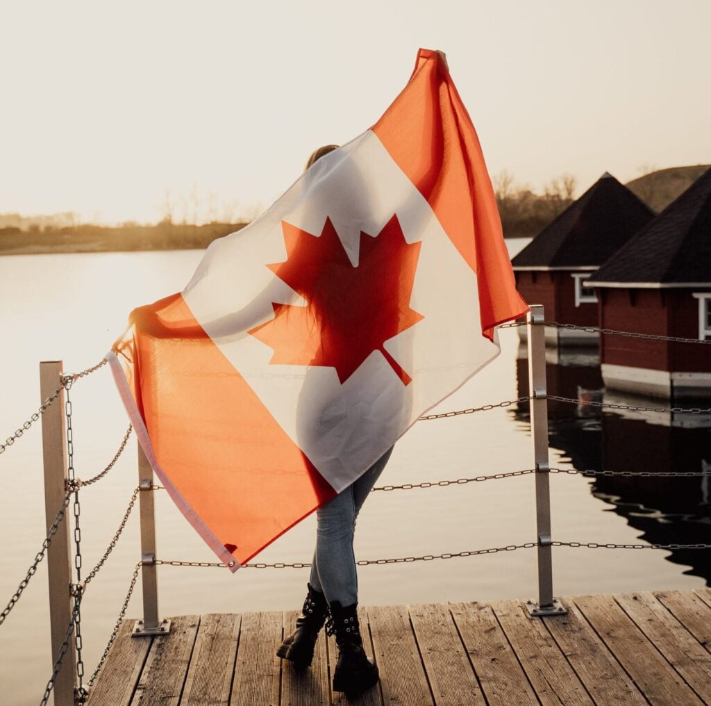 Woman with Canadian flag on back on dock after immigrating to Canada